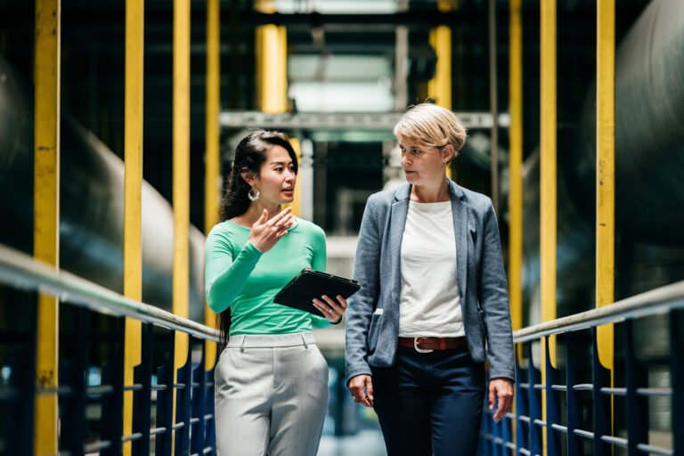 Ey two women discussing work among large machinery.jpg
